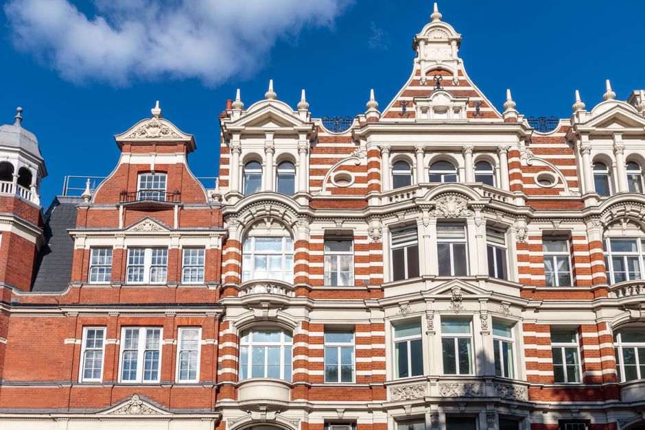 A multi-story red brick residential building with black wrought iron balconies and white-framed windows, situated on Davies Street West in Mayfair. The building features decorative stone accents aroun